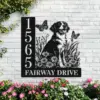 Black metal house sign on white brick wall showing address 1565 and the words FAIRWAY DRIVE with a sitting dog, daisies and two butterflies, flowers planted below.