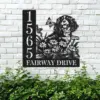 Black metal house sign mounted on a white brick wall showing numbers 1565 and text "FAIRWAY DRIVE" with a dog, flowers and butterflies, greenery below