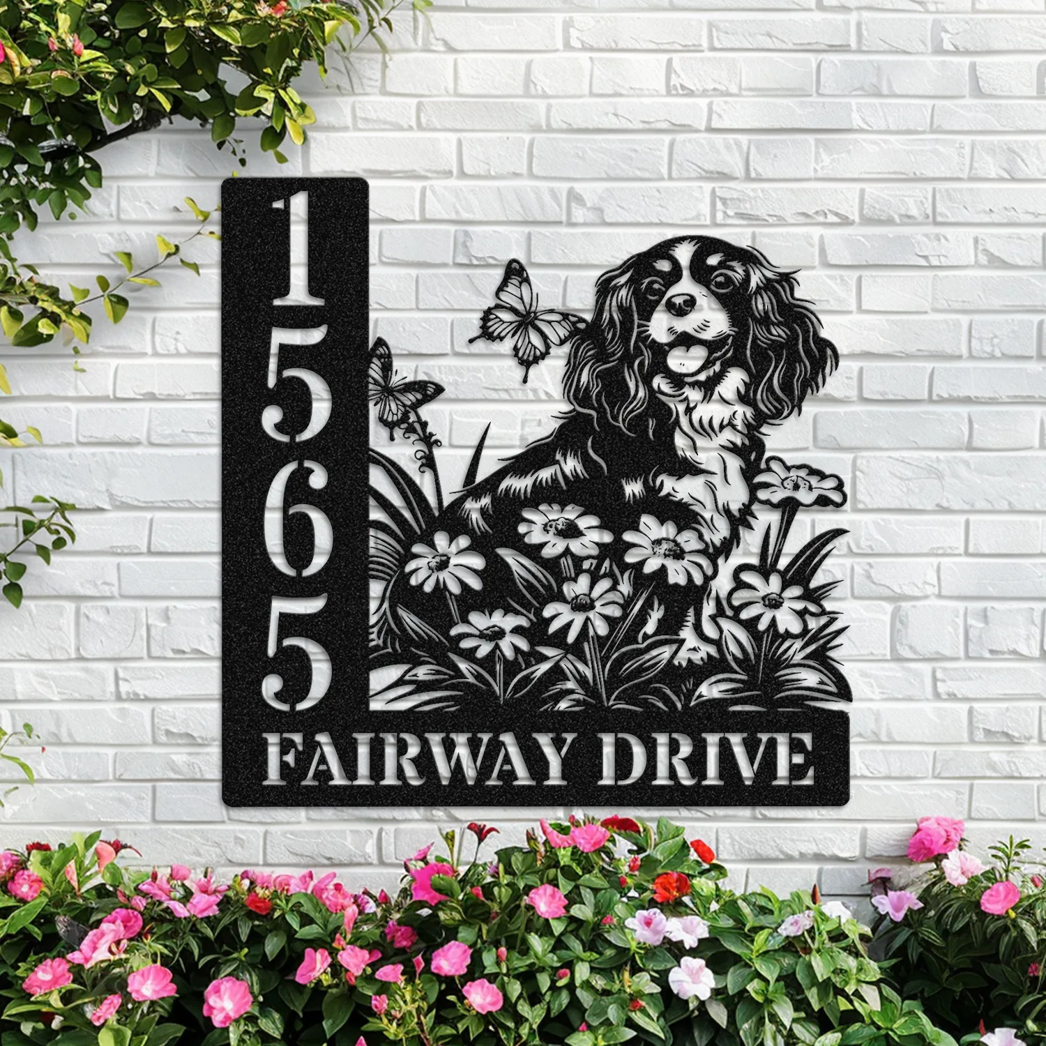 Cavalier-King-Charles-Spaniel-Sitting-with-Butterfly-4-2 Black metal house sign mounted on a white brick wall showing address numbers 1565 and text 'FAIRWAY DRIVE' with a dog illustration, flowers, butterflies and pink garden blooms below