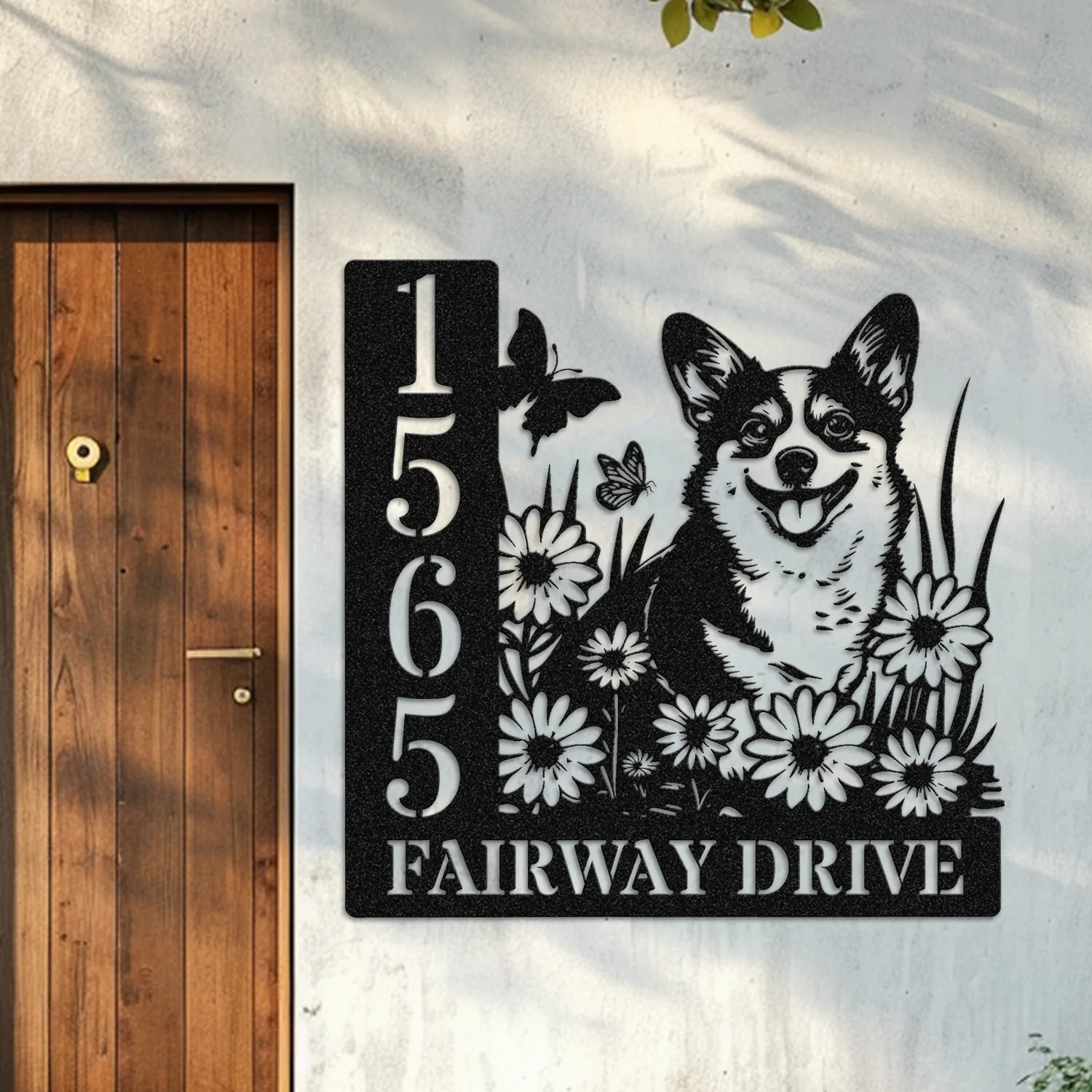 Corgi-Sitting-with-Butterfly-1 Black metal house sign mounted next to a wooden door showing address 1565 and text FAIRWAY DRIVE with a smiling corgi among daisies and butterflies