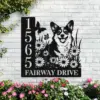 Corgi-Sitting-with-Butterfly-4 Black metal address sign mounted on a white brick wall showing numbers 1565, text ‘FAIRWAY DRIVE’, a smiling corgi among daisies with butterflies, surrounded by flowering plants