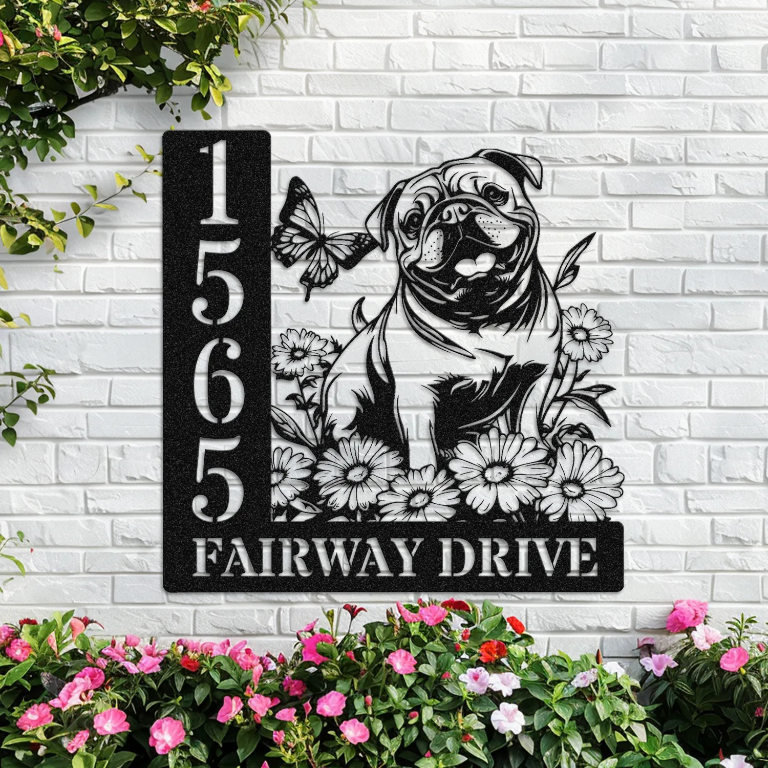 English-Bulldog-Sitting-with-Butterfly-4 Black metal house sign mounted on white brick showing numbers 1565 and text FAIRWAY DRIVE with a pug illustration, flowers and a butterfly, garden plants below