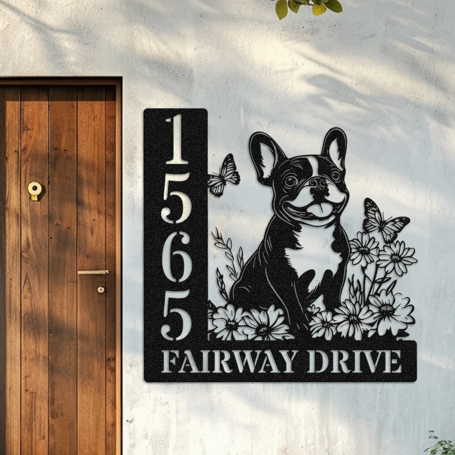 French-Bulldog-Sitting-with-Butterfly-1 Black metal house sign on exterior wall next to wooden door showing address 1565 and text FAIRWAY DRIVE with a happy French bulldog, flowers and butterflies