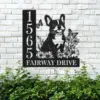 French-Bulldog-Sitting-with-Butterfly-2 Black metal house sign mounted on a white brick wall showing address 1565 and text FAIRWAY DRIVE with a sitting French bulldog, flowers, and butterflies above green shrubs.