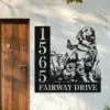 Black metal house number sign reading 15655 and FAIRWAY DRIVE with cutout design of a dog, flowers and butterflies mounted beside a wooden door on an exterior wall