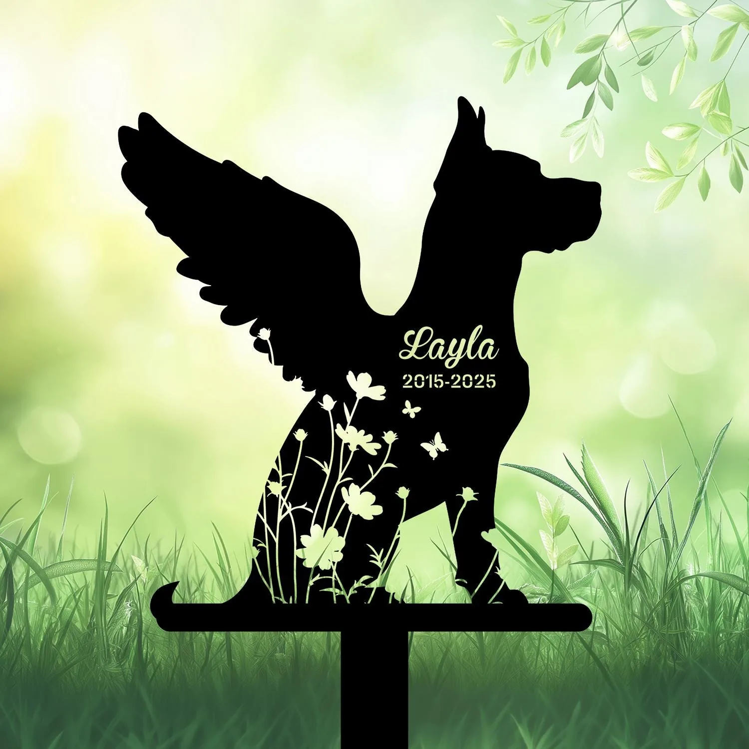 Black dog silhouette memorial stake with wings and floral cutouts, text “Layla 2015-2025” against a soft green garden background