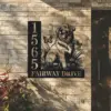 Black metal house sign mounted on a light brick wall showing numbers 1565 and text FAIRWAY DRIVE with a sitting dog, butterflies, and flowers design
