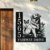 Black metal house sign mounted by a wooden front door showing numbers 1565 and the street name FAIRWAY DRIVE with a sitting dog, butterflies, and flowers design