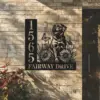 Black metal house sign mounted on a light brick wall showing address 1565 and the words FAIRWAY DRIVE with a cutout design of a happy dog, flowers and butterflies