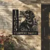 Black metal house sign mounted on a brick exterior showing numbers 1565, the text 'FAIRWAY DRIVE', and a dog with flowers and a butterfly motif