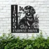 Black metal house sign mounted on a white brick wall showing number 1565 and text "Fairway Drive" with a dog, flowers, and a butterfly design above green shrubbery