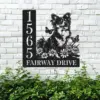 Black metal house sign mounted on a white brick wall showing numbers 1565 and text FAIRWAY DRIVE with a cheerful dog, flowers and butterflies above green shrubs