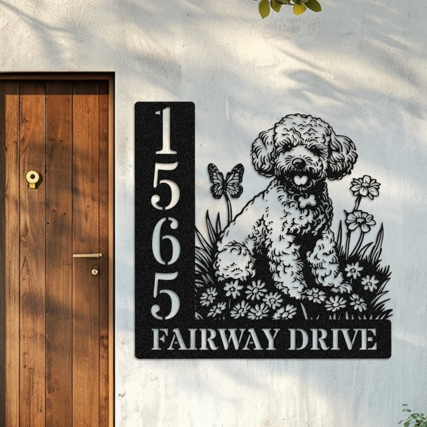 Black metal house sign mounted next to a wooden door showing address numbers 1565 and the street name FAIRWAY DRIVE with a decorative puppy, flowers and butterfly design