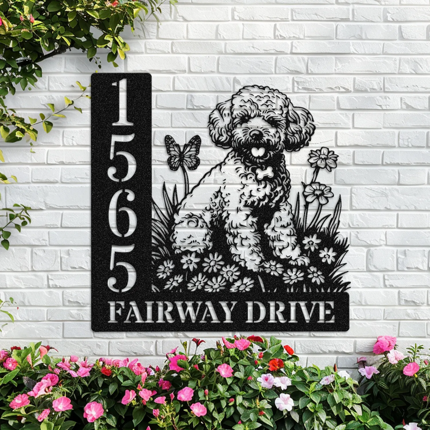 Black metal house sign mounted on a white brick wall with address numbers 1565 and text 'FAIRWAY DRIVE' beside a floral poodle silhouette, surrounded by pink flowers and green vines.