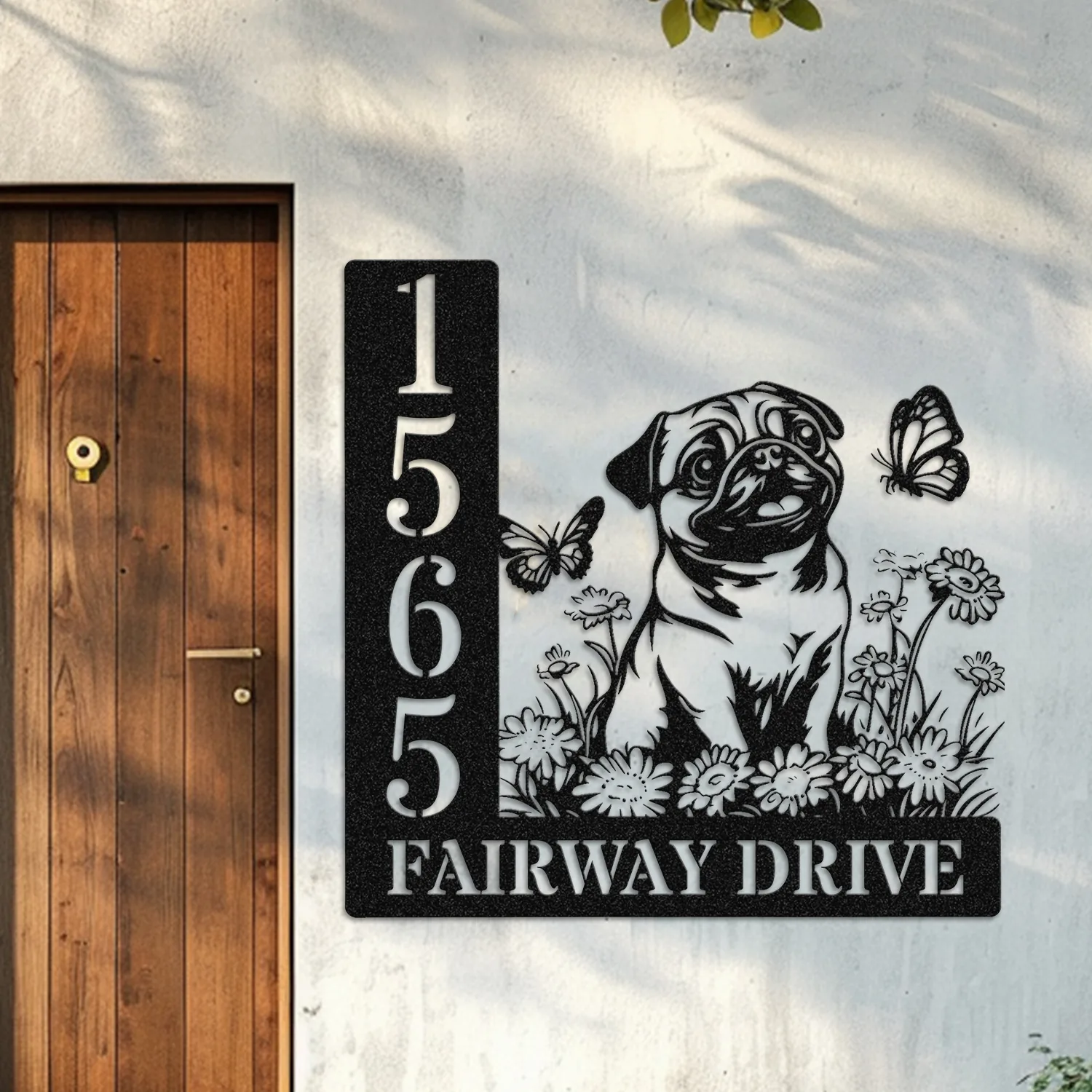 Pug-Sitting-with-Butterfly-1 Black metal house sign on exterior wall beside wooden door showing numbers 1565, text ‘FAIRWAY DRIVE’ and a pug among flowers with butterflies