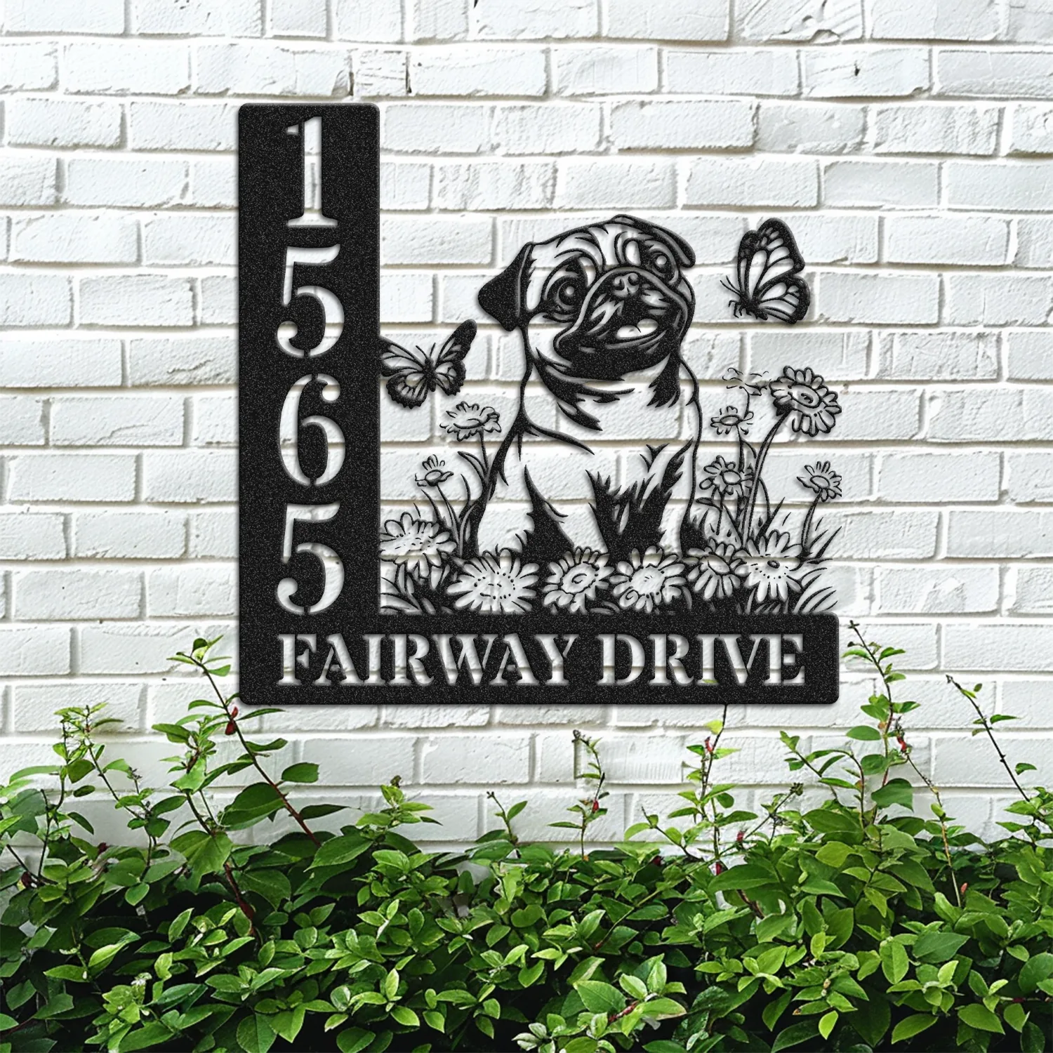 Pug-Sitting-with-Butterfly-2 Black metal house sign mounted on a white brick wall showing numbers 1565 and text ‘FAIRWAY DRIVE’ with a pug illustration, flowers, and butterflies above green shrubs.