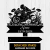 Black metal memorial sign showing a motorcyclist on a sportbike surrounded by flowers, text reading "IN LOVING MEMORY OF", placeholder "Name" and dates "1970-2024", with detached stakes on a light wood background