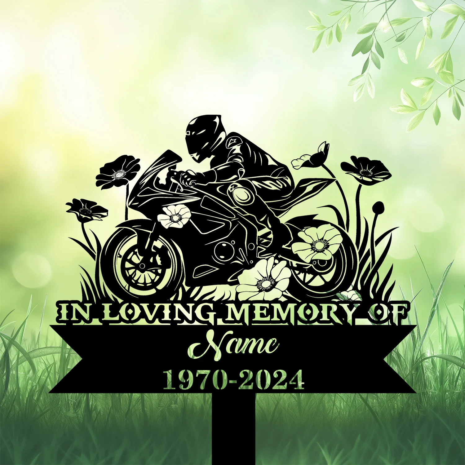 Black silhouette memorial sign of a motorcyclist on sport bike with flowers, text reading "IN LOVING MEMORY OF" and placeholder name and dates 1970-2024 on green grassy background