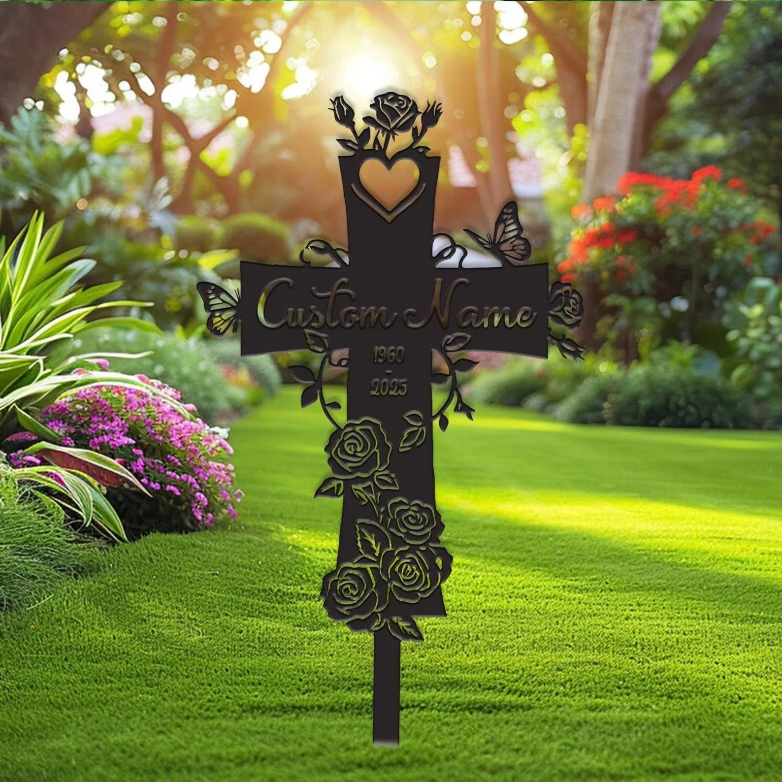 Decorative black metal memorial cross stake with heart, roses and butterflies reading "Custom Name" and years in a sunlit garden lawn