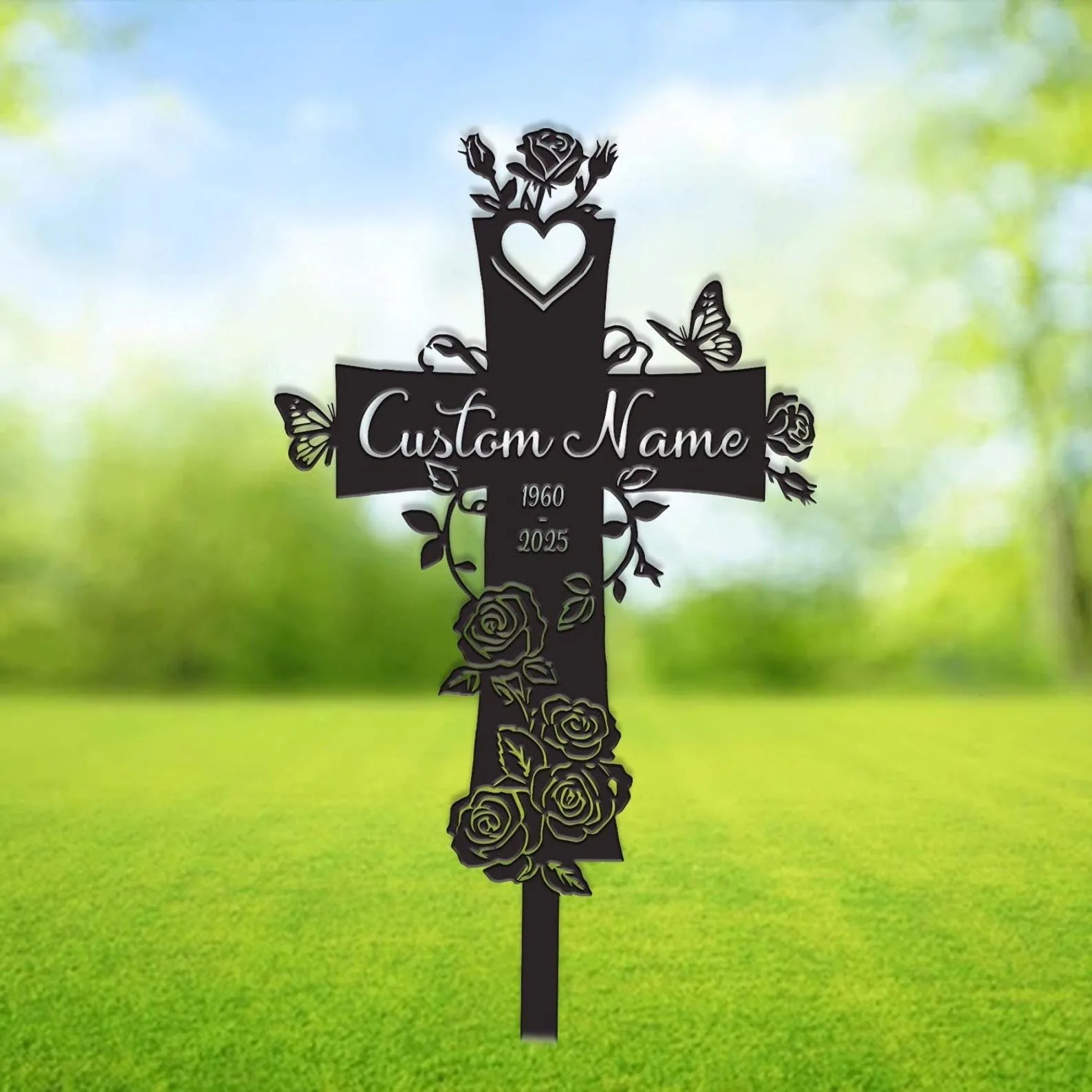 Metal cross lawn stake with roses, butterflies and a heart cutout, showing placeholder text "Custom Name" and dates 1960–2025 against a blurred green outdoor background