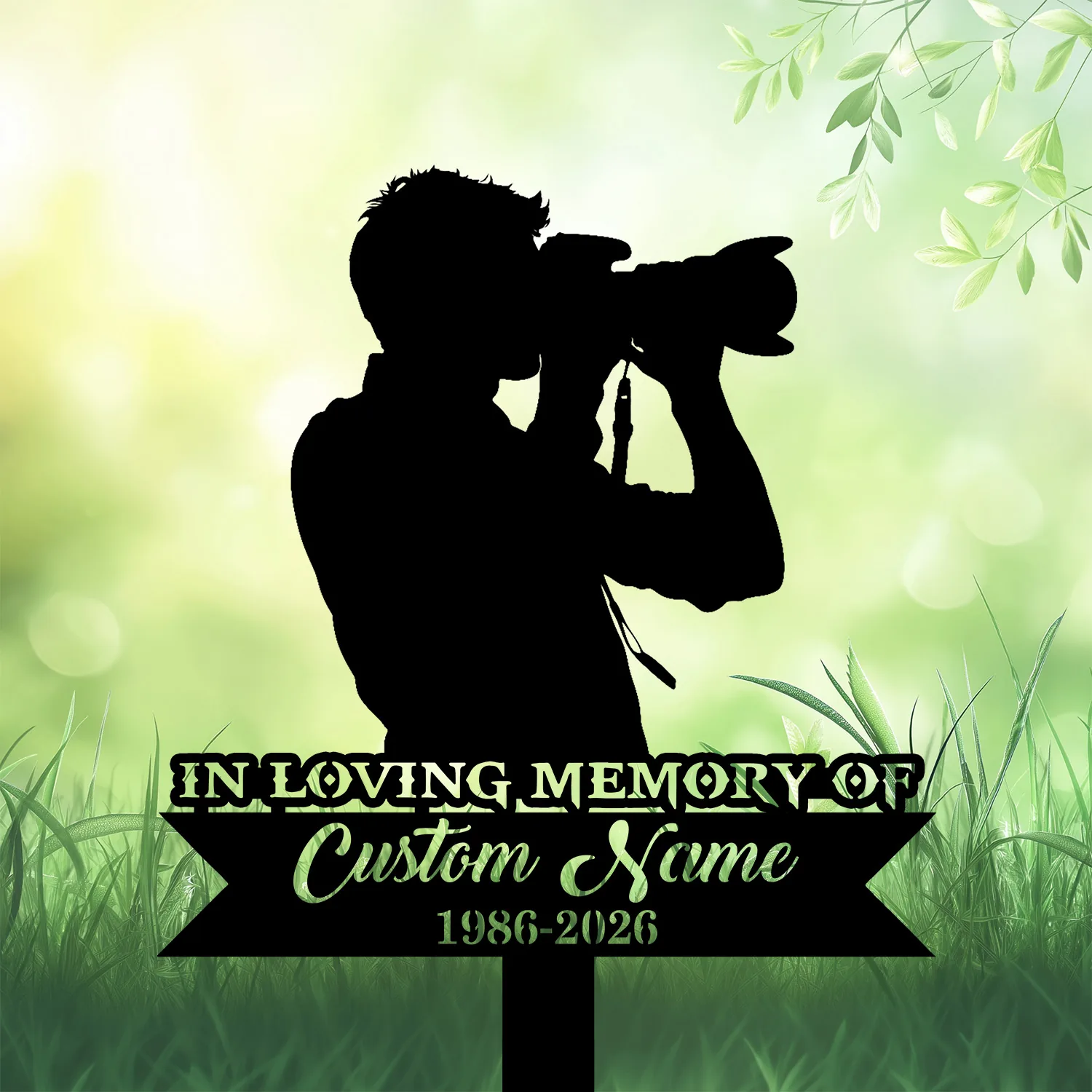 Black silhouette of a photographer with camera on a memorial sign reading "IN LOVING MEMORY OF Custom Name 1986-2026" against a soft green leafy background