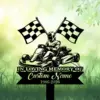 Black silhouette memorial sign of a go-kart driver with crossed checkered flags above and text reading "In Loving Memory of Custom Name 1986-2026" against a green grassy background