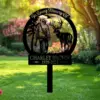 Black metal memorial yard sign reading "In Loving Memory Of" and "Charley Brown 1939-2025" showing a hunter with rifle and a stag silhouette against a garden lawn background