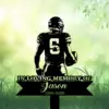 Silhouette of a football player wearing jersey number 5 holding a helmet above a memorial sign reading "In Loving Memory of Jason 1990-2026" on a grassy, green blurred background