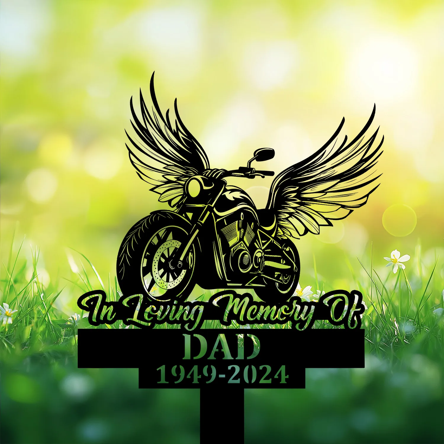 Black silhouette memorial sign of a winged motorcycle reading "In Loving Memory Of" and "DAD 1949-2024" against a sunny grassy background