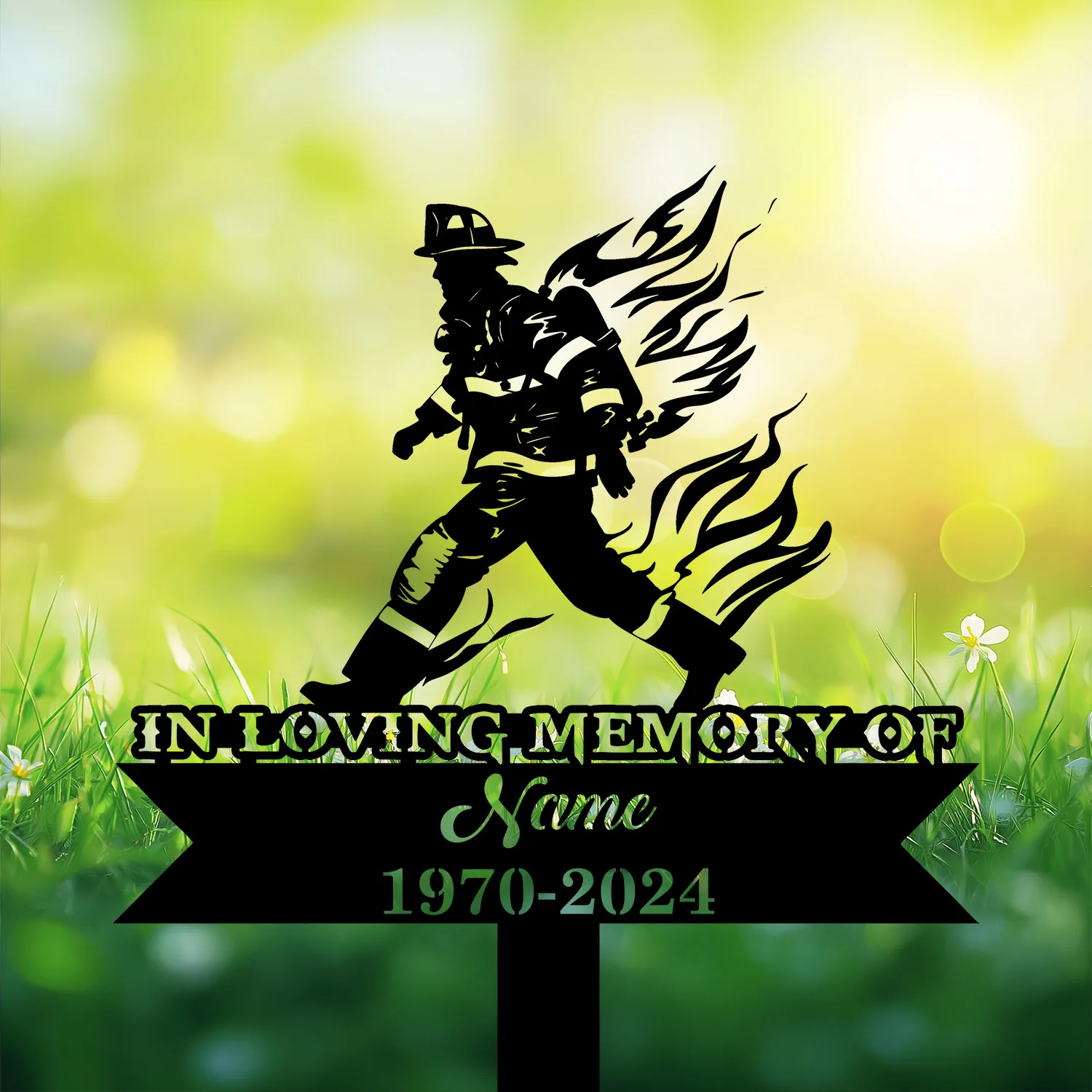 Silhouette memorial garden sign showing a firefighter walking with stylized flames, text reading "IN LOVING MEMORY OF" with placeholder Name and dates 1970-2024 against a sunlit grassy background
