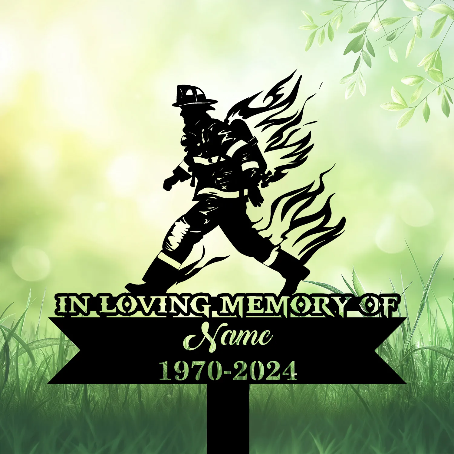 Black silhouette memorial yard sign of a firefighter with stylized flames, text reading "IN LOVING MEMORY OF", placeholder "Name" and dates "1970-2024" against a soft green grassy background