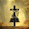 Black memorial cross with draped cloth, floral decoration and plaque reading “In Loving Memory of Custom Name 1955 - 2025” against a sunlit forest path background