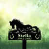 Black silhouette memorial sign of a resting horse over flowers with name "Stella" and years "2012-2023" against a soft green grassy background