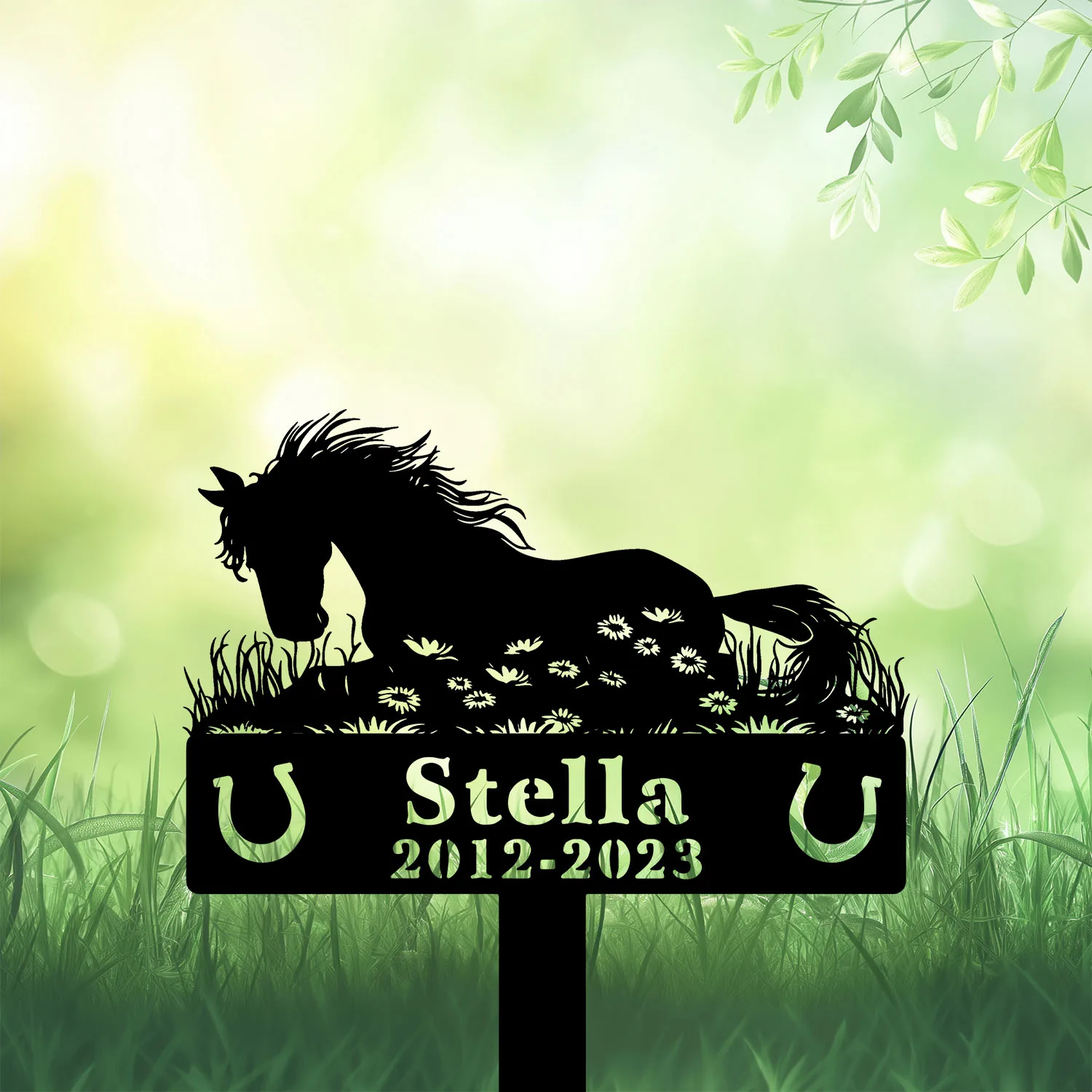 Black silhouette memorial sign of a resting horse over flowers with name "Stella" and years "2012-2023" against a soft green grassy background
