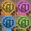 Round LED wall sign of two embracing skeletons with rose wreath and the names "LIAM & EMMA" lit in yellow, pink, blue, and green above a decorated shelf