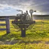Metal memorial sign in a sunny field showing a tractor, windmill and wings with text “In Loving Memorial Of Russel Smith 1963 - 2025” mounted near a wooden fence