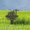Black metal memorial sign with a tractor and windmill silhouette reading "In Loving Memorial Of Russel Smith 1963 - 2025" staked in a grassy field