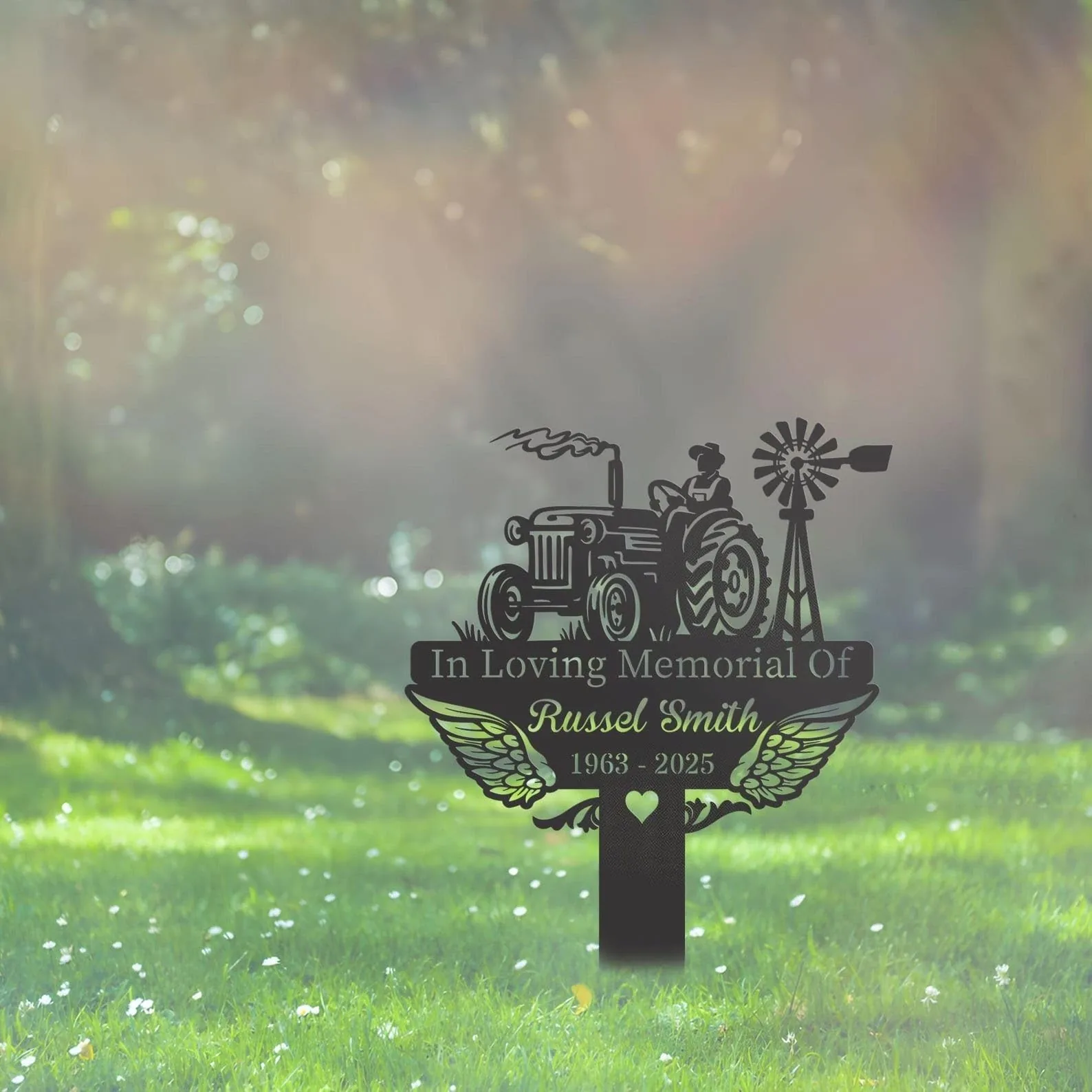 Memorial metal yard sign with tractor and windmill silhouette, wings and text reading "In Loving Memorial Of Russel Smith 1963 - 2025" staked in a sunlit grassy lawn