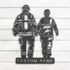 Metal wall art of two firefighters holding hands walking away, cutout design with plate reading "CUSTOM NAME", on white wood background
