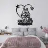 Black metal wall art above bed reading 'MARA & DAVID 2022' with frog couple inside a heart and text 'TOGETHER UNTIL WE CROAK' in modern bedroom