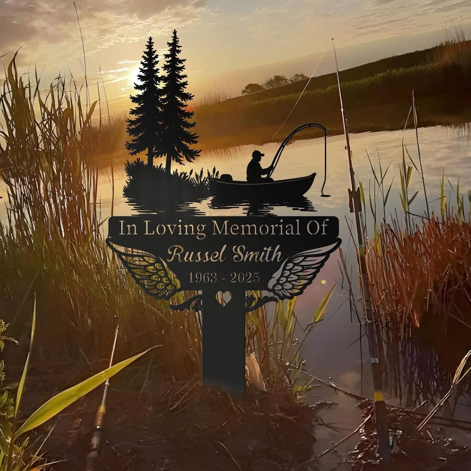 Metal memorial sign with fishing silhouette and pine trees reading "In Loving Memorial Of" and name over a sunset pond with reeds and fishing rods
