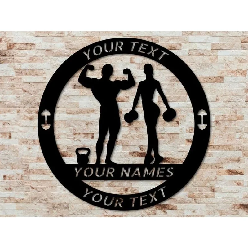 Black metal circular sign on a light brick wall showing male and female fitness silhouettes with kettlebell and dumbbells, placeholder text reading YOUR TEXT and YOUR NAMES