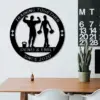 Black round metal wall sign reading 'Training Together' and 'Denis & Emily Since 2020' with silhouettes of a man flexing and a woman holding dumbbells, hung above a desk