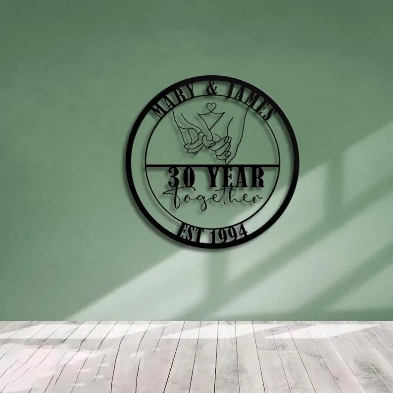Black circular metal wall sign reading 'Mary & James' with linked pinky hands, '30 Year together' and 'Est 1994' mounted on a mint green wall over light wood floor