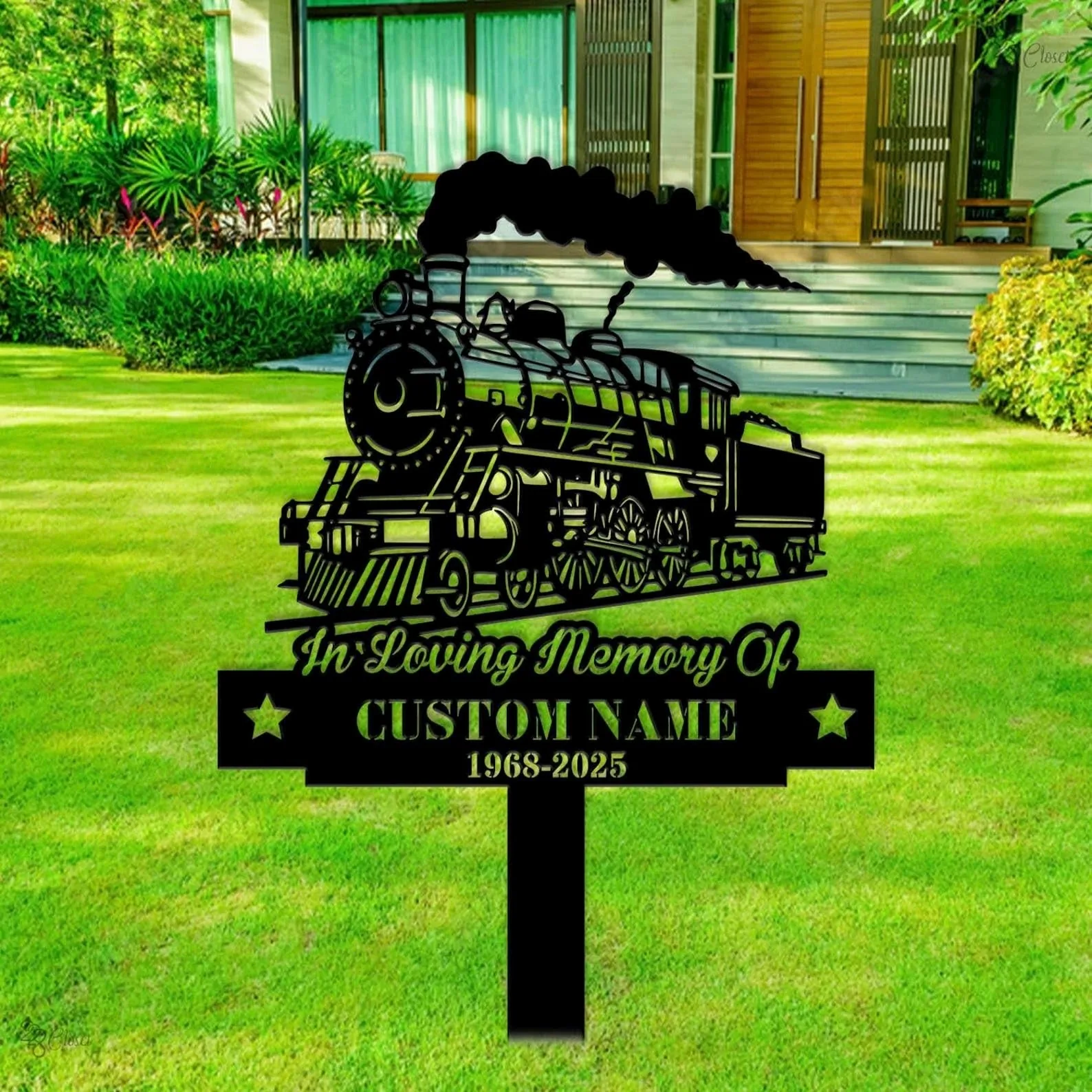 style-18.-Train-Memorial-3 Black metal memorial yard sign shaped like a steam locomotive with smoke, reading "In Loving Memory of" and placeholder "CUSTOM NAME 1968-2025" staked in a green lawn in front of a modern house