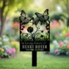 Black metal memorial garden stake with butterfly and flower cutouts reading "In Loving Memory of Henry Hoyer 12/1/1988 - 11/15/2024" against a blurred colorful garden background