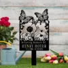 Black metal memorial garden stake with butterflies and flowers reading "In Loving Memory Of HENRY HOYER 12/1/1988 - 11/15/2024" placed on grass with watering can, roses and tulips nearby
