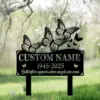 Black metal memorial yard sign with decorative butterflies, placeholders reading "CUSTOM NAME" and dates "1945-2025" against a soft-focused spring garden background