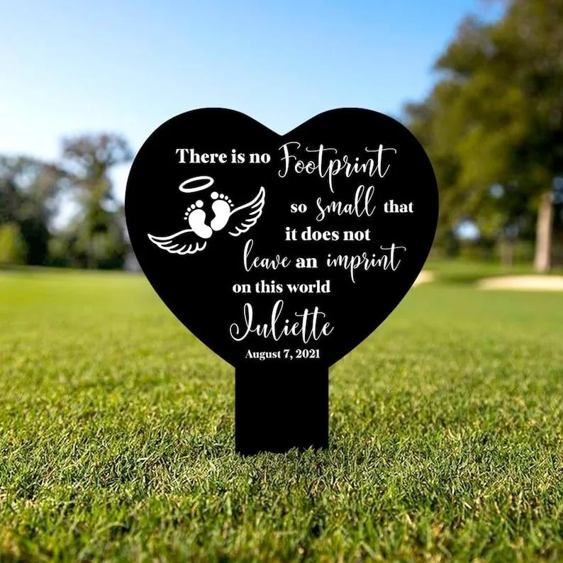 Black heart-shaped lawn sign reading "There is no footprint so small that it does not leave an imprint on this world" with baby footprints, name Juliette and date August 7, 2021, placed on grass outdoors