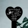 Black heart-shaped memorial sign with white text reading a remembrance quote, baby footprints with wings and halo, name "Juliette" and date August 7, 2021, displayed against a textured light wall near a plant.